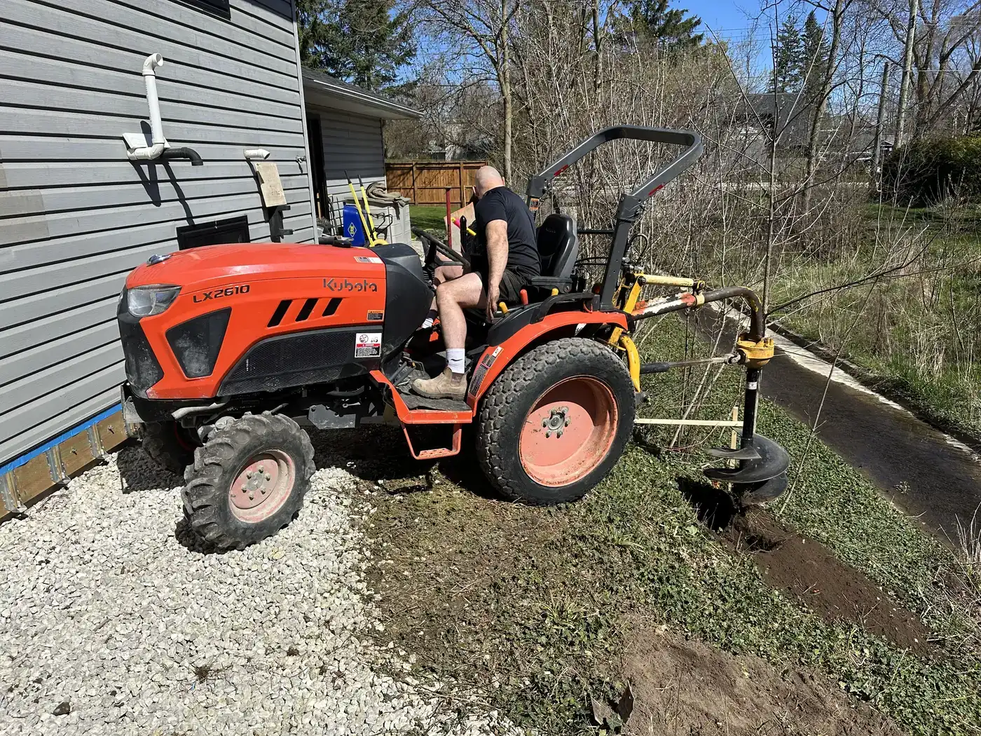 Tractor mounted auger digging a post hole beside a house
