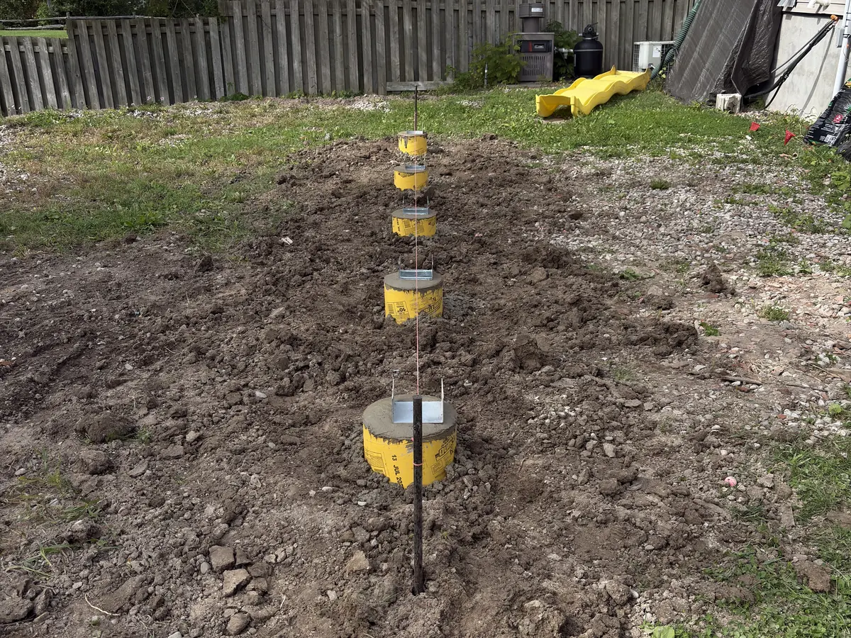Row of poured deck pier sonotubes with steel post saddles set in a backyard
