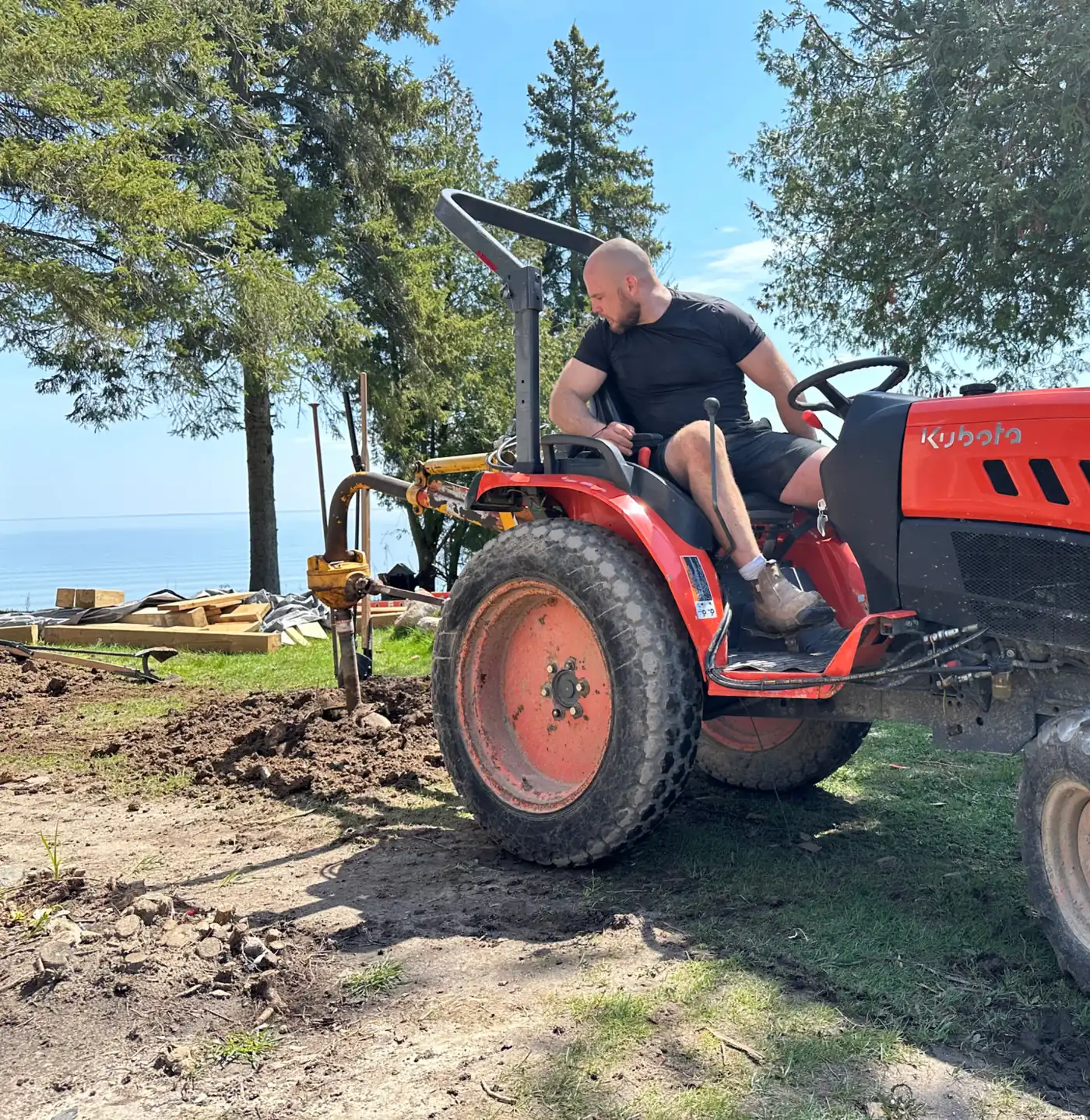 McNic Holes operator on a red tractor digging post holes near the water